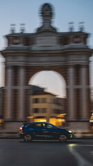 Panning foto, con macchina blu che percorre la strada davanti a un arco storico