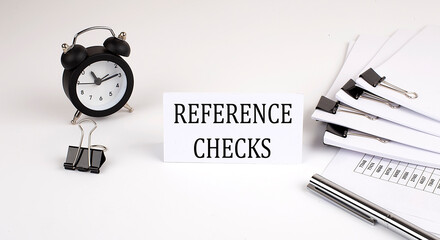 Card with text REFERENCE CHECKS on a white background, near office supplies and alarm clock. Business concept.