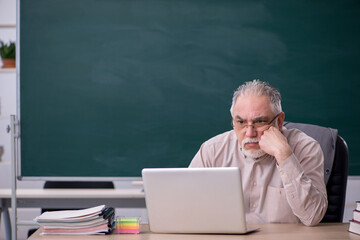 Old male teacher in front of blackboard in telestudy concept