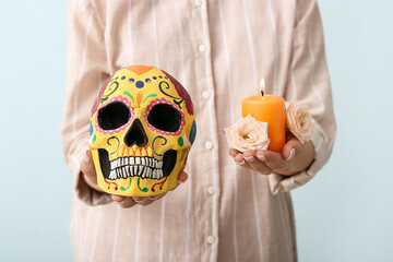 Woman with painted human skull for Mexico's Day of the Dead (El Dia de Muertos), flowers and candle on light background