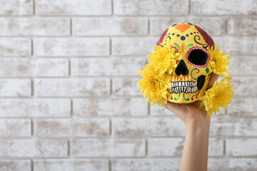 Hand with painted human skull for Mexico's Day of the Dead (El Dia de Muertos) and flowers on brick...