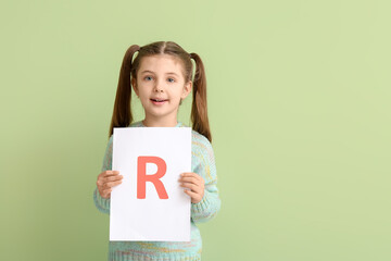 Fototapeta na wymiar Little girl holding paper sheet with letter R on color background