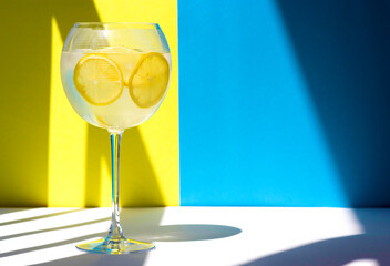 Refreshing lemon drink in a glass on a yellow and blue background. Hard shadows
