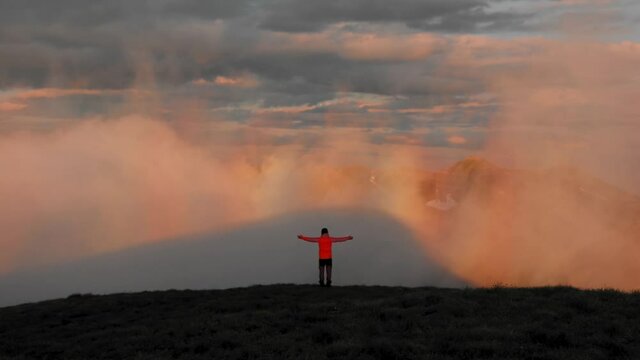 A hiker holding his hands out at the top of the Fagaras mountains at sunset with fog hovering in front of him