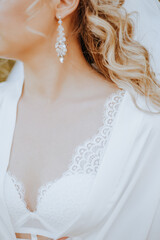 The bride puts on beautiful wedding earrings. Girl with hairstyle with curls wears jewelry accessories