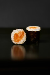 Two sushi roll lies on a mirror black surface.