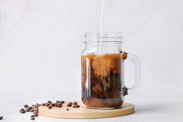 Pouring of milk into mason jar with hot coffee and beans on white background