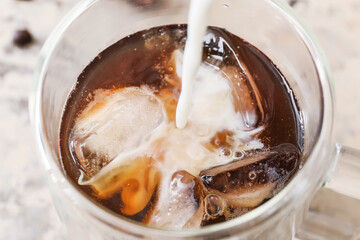 Pouring of milk into glass with hot coffee on light background, closeup