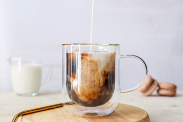 Pouring of milk into cup with hot coffee on light background