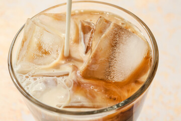 Pouring of milk into glass of hot coffee with ice on light background, closeup