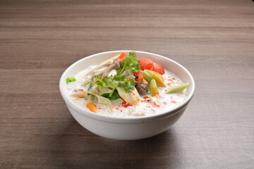 cook hot and spicy white coconut curry laksa soup with mushroom and mixed vegetables in white bowl on wood background asian halal vegan menu