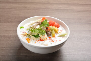 cook hot and spicy white coconut curry laksa soup with mushroom and mixed vegetables in white bowl on wood background asian halal vegan menu