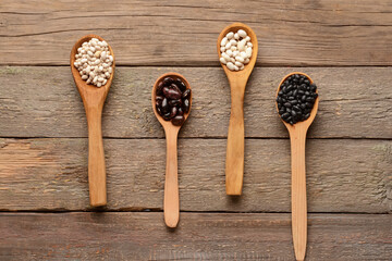Spoons with different types of beans on wooden background