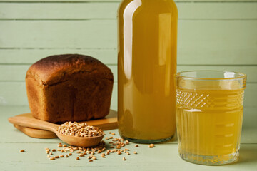 Glass and bottle of fresh kvass on color wooden background