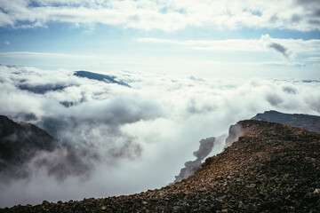 Atmospheric scenery on top of mountain ridge above clouds to vertex in thick low clouds. Minimalist view from precipice edge over clouds. Beautiful landscape with mountain range over dense clouds.