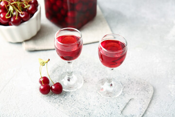 Glasses of sweet cherry wine on light background