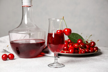 Decanter and glass of sweet cherry wine on light background