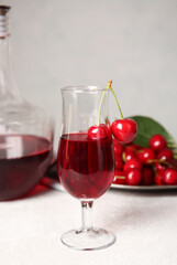Glass of sweet cherry wine on light background