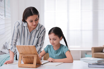 Mother helping her daughter doing homework with tablet at home