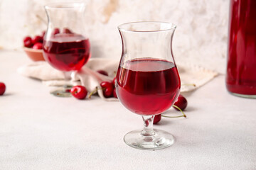 Glasses of sweet cherry wine on light background
