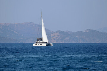 Fototapeta na wymiar One-masted sailing yacht in the sea. White sailboat on misty mountains background