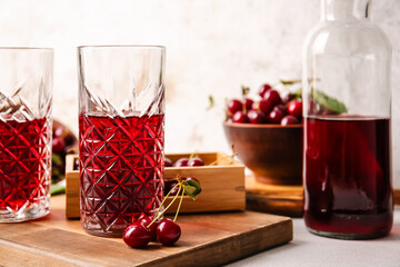 Glasses of sweet cherry wine on light background