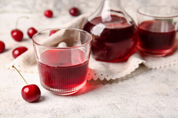 Glasses and decanter of sweet cherry wine on light background, closeup