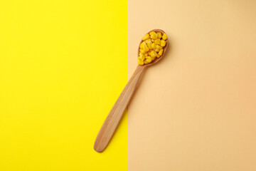 Spoon with corn seeds on two tone background