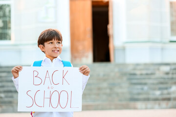 Cute little boy holding poster with text BACK TO SCHOOL outdoors