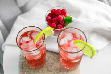 Glasses of tasty lemonade and bowl with raspberry on table in room
