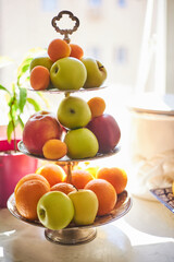 Three tier fruit bowl, tray stand, holding many apples, oranges and peaches waiting to be eaten