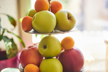 Three tier fruit bowl, tray stand, holding many apples, oranges and peaches waiting to be eaten