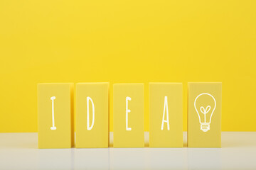 Concept of idea, creativity, start up or brainstorming. The word idea and bulb drawn on yellow toy blocks against bright yellow background with copy space.