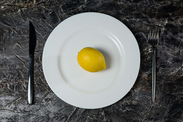large lemon on a white plate on a dark background with cutlery fork and knife
