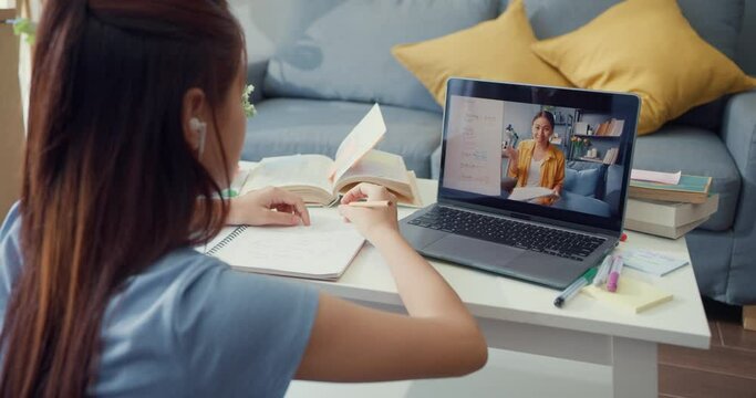 Young Asia girl with casual use computer laptop video call learn online with teacher write lecture notebook living room at house. Isolate education online e-learning coronavirus pandemic concept.