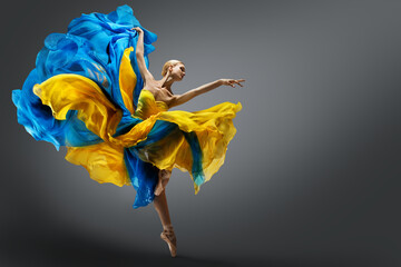 Beautiful Woman Ballet Dancer Jumping in Air in Colorful Fluttering Dress. Graceful Ballerina Dancing in Yellow Blue Gown over Gray Studio Background - obrazy, fototapety, plakaty