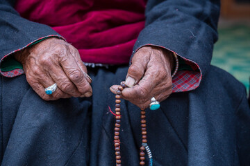 Old Tibetan woman holding buddhist rosary in Hemis monastery, Ladakh, India. Hand and rosary