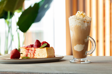 Glass of latte coffee and piece of strawberry cheesecake on gray table