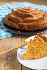 Top view of yogurt sponge cake on checkered cloth, with portion on white plate with wooden fork, selective focus, on wooden table, vertical