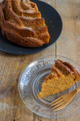 Aerial view of half yogurt cake with portion on transparent plate with wooden fork, on wooden table, in vertical