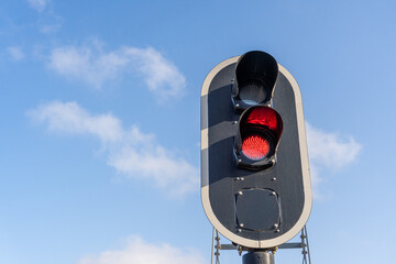 Close-up of a railway traffic light, with a red light and the blue sky in the background at sunset.