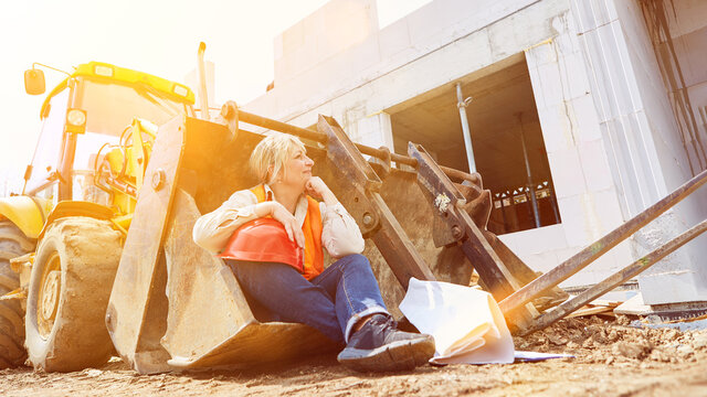 Arbeiterin auf Baustelle sitzt in Schaufel von Bagger bei Pause