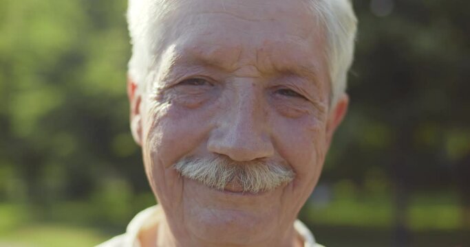 Bokeh close up portrait of happy senior man looking at camera outdoors