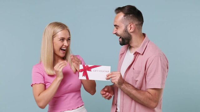 Happy young couple two friends family man woman in pink clothes together give mockups of gift certificate coupon voucher card flyer isolated on pastel plain light blue color background studio portrait
