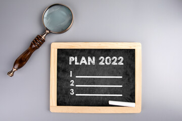 2022 plan on chalkboard, goal setting and priority in coming year. Magnifying glass on a gray table