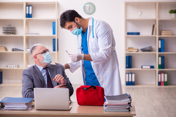 Young male doctor visiting old businessman at workplace