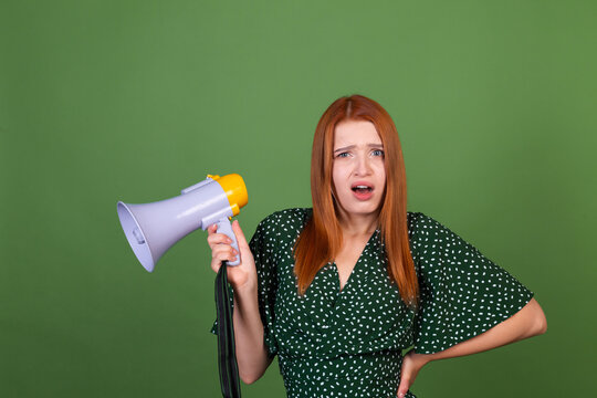 Young red hair woman on green background with megaphone confused having no clue