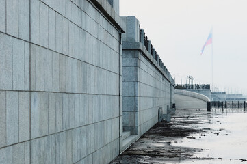 The lower level of the flooded city embankment. Russian flag in the fog. Summer early morning.