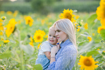 Mom with a little daughter 3 years old in a sunflower field. Summer sunset. Family. Happiness.