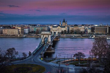 Budapest, Hungary - The Szechenyi Chain Bridge at sunset decorated with national flags celebrating the 15th of March 1848 civic revolution day. St.Stephen's Basilica at background with magenta sky